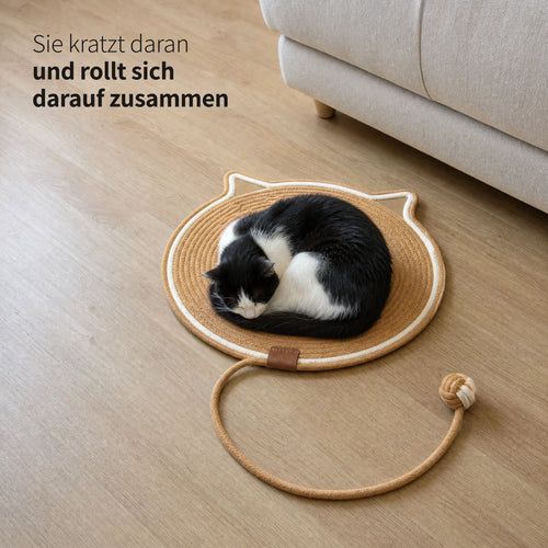 Schwarz-weiße Katze schläft eingerollt auf der Instinkt Matte in Karamell neben dem Sofa: Sie kratzt daran und rollt sich darauf zusammen